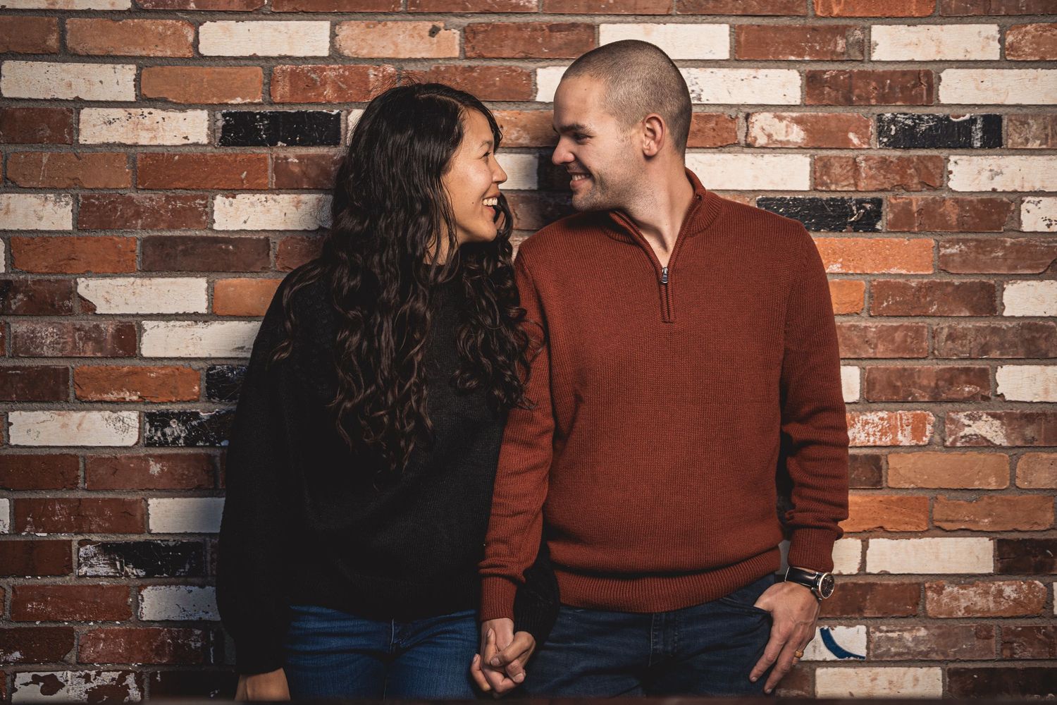 Couple shares intimate moment against rustic brick wall background.