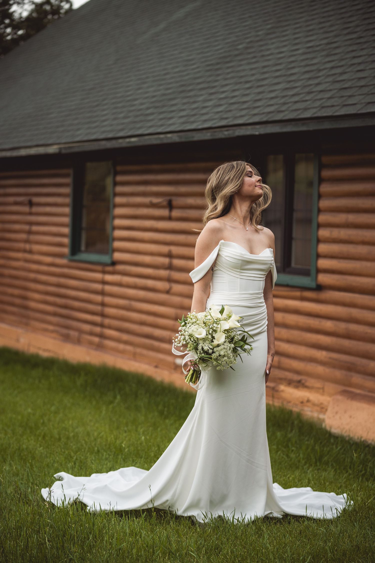 Elegant white wedding dress displayed against rustic log cabin siding.
