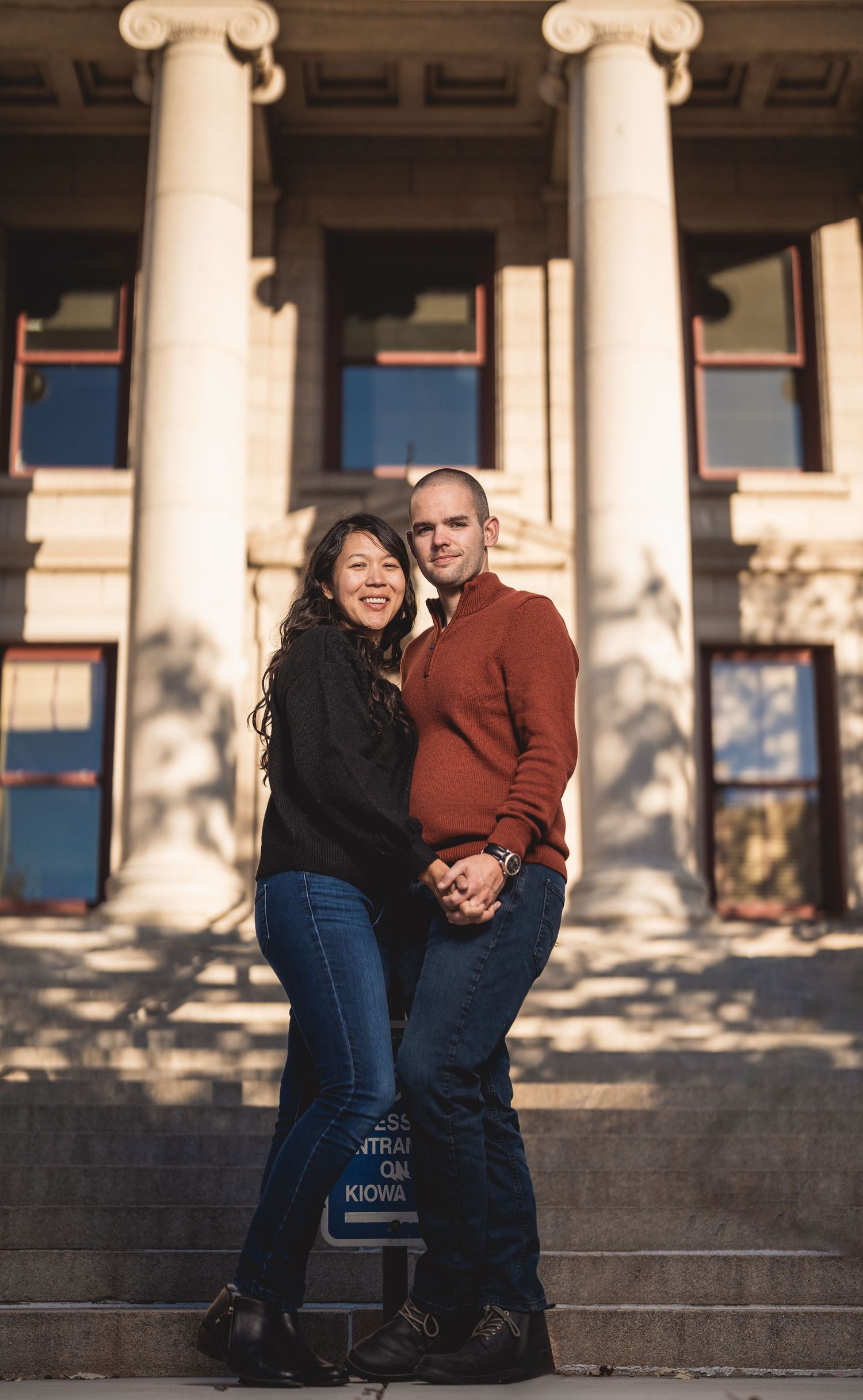 Couple sharing a romantic moment on stone steps in front of classical columns during a sunset photoshoot.