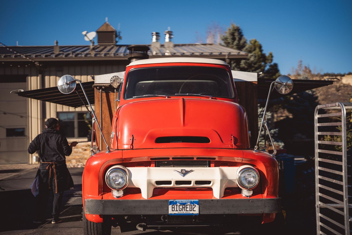 Vintage red truck parked against blue sky and mountains in rustic setting.