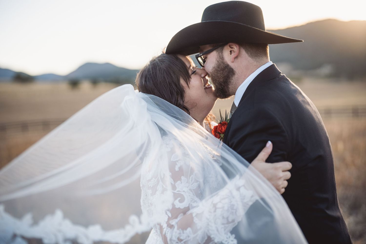 Romantic sunset wedding portrait with flowing veil in mountain landscape.