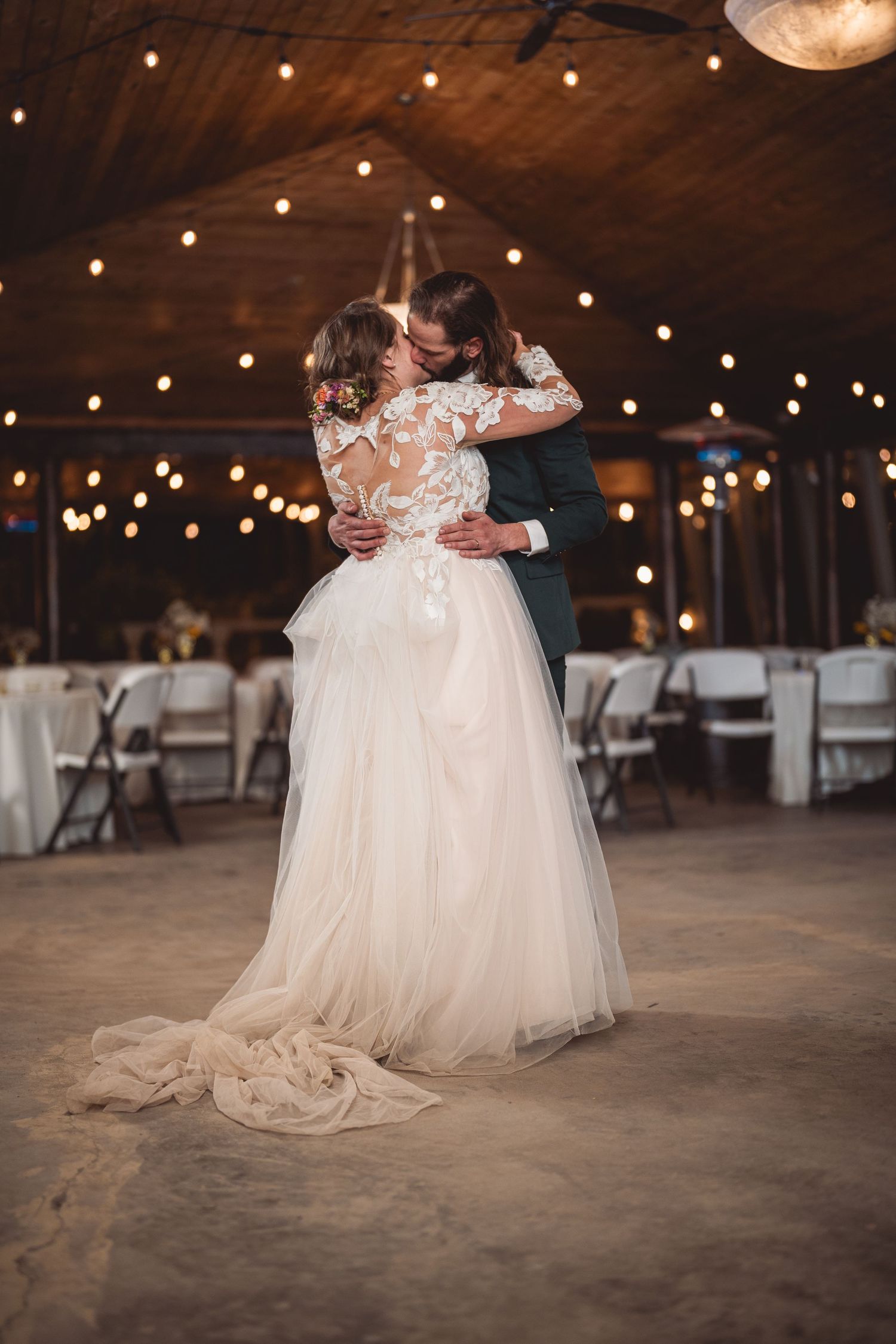 Couple dancing together in a rustic wedding venue decorated with twinkling string lights.