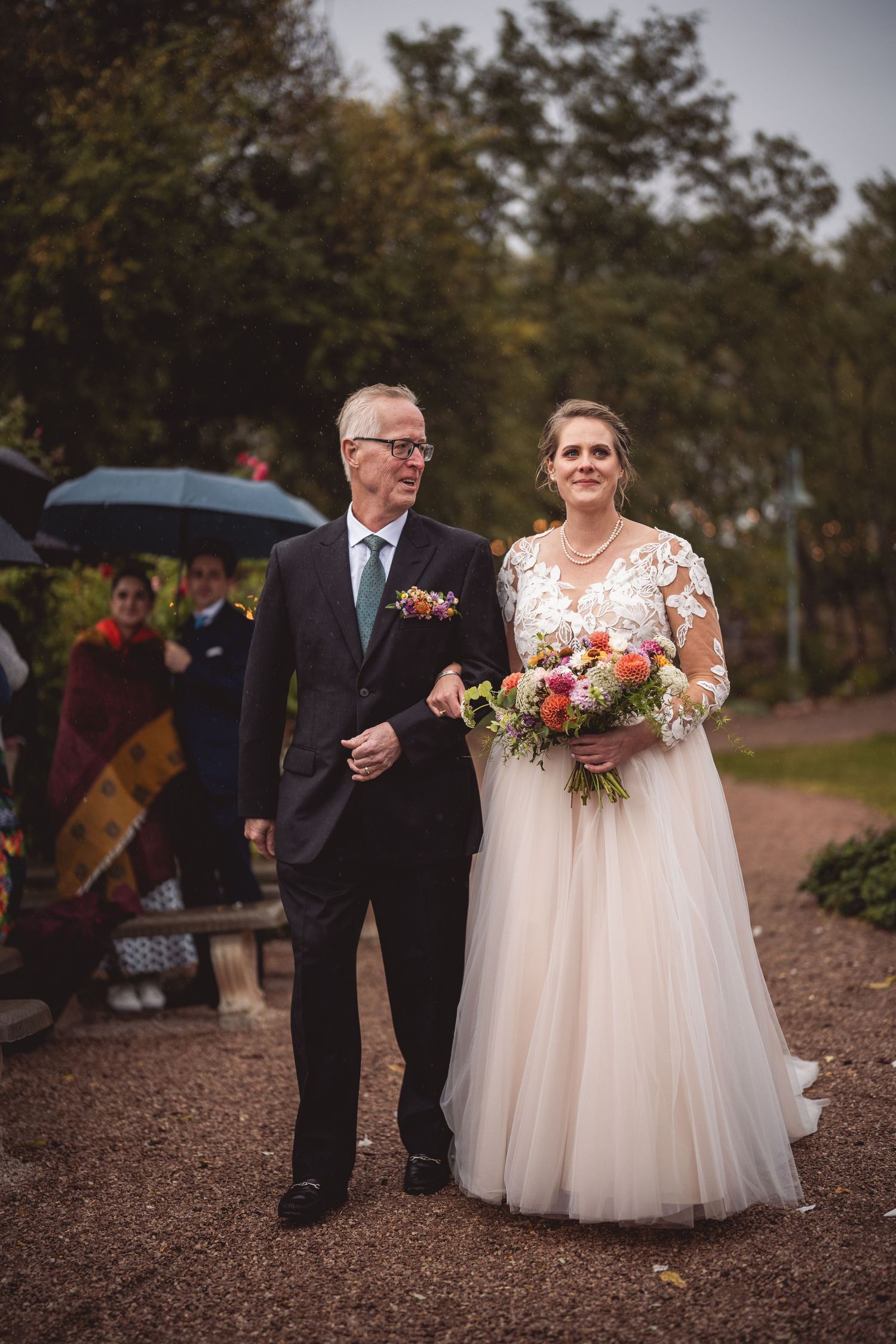 Wedding party walks along gravel path with florals and string light decorations.