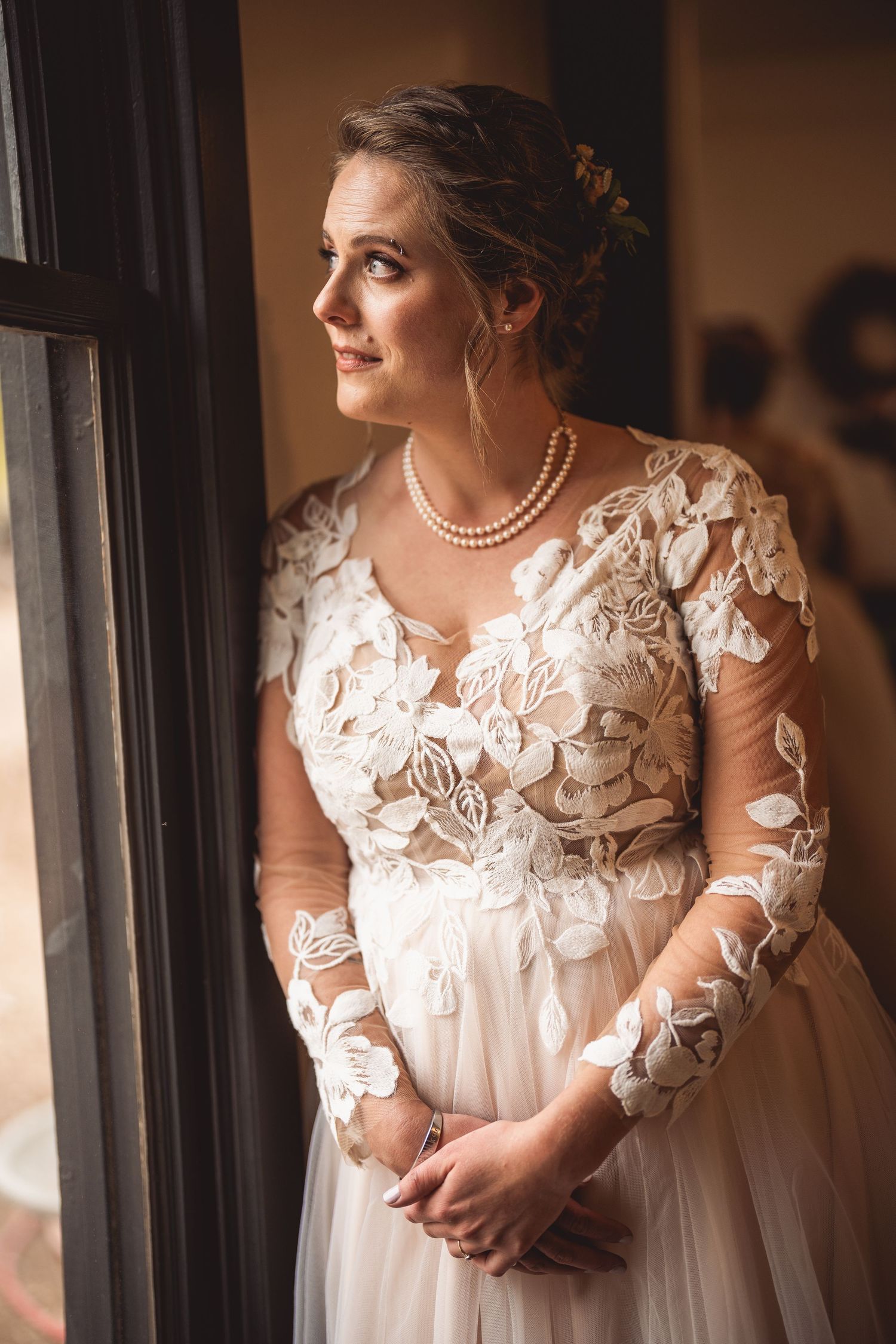 Natural light portraits capture bride in elegant lace dress with pearl necklace near window.