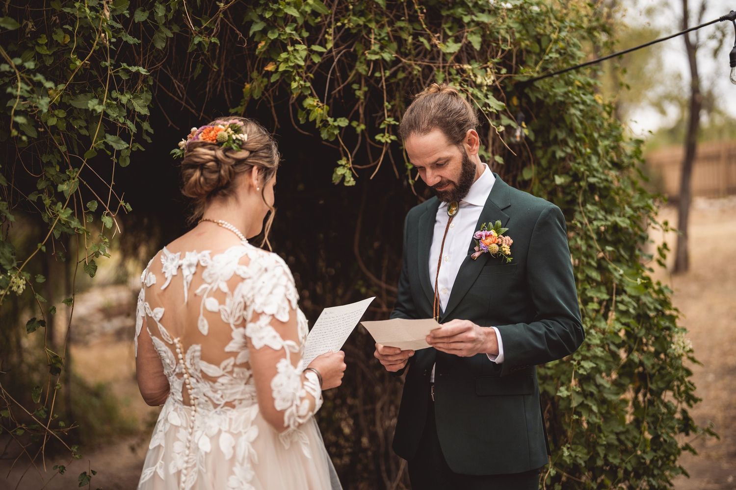 Couple exchanges vows during intimate outdoor ceremony surrounded by greenery.