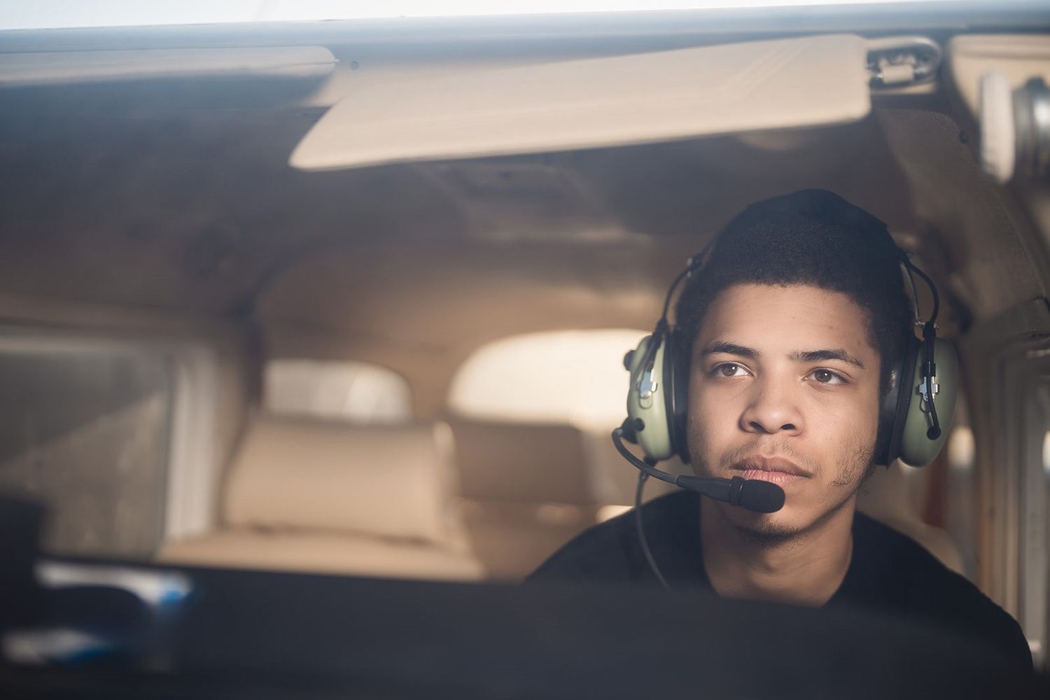 Pilot wearing headset inside cockpit of small aircraft.
