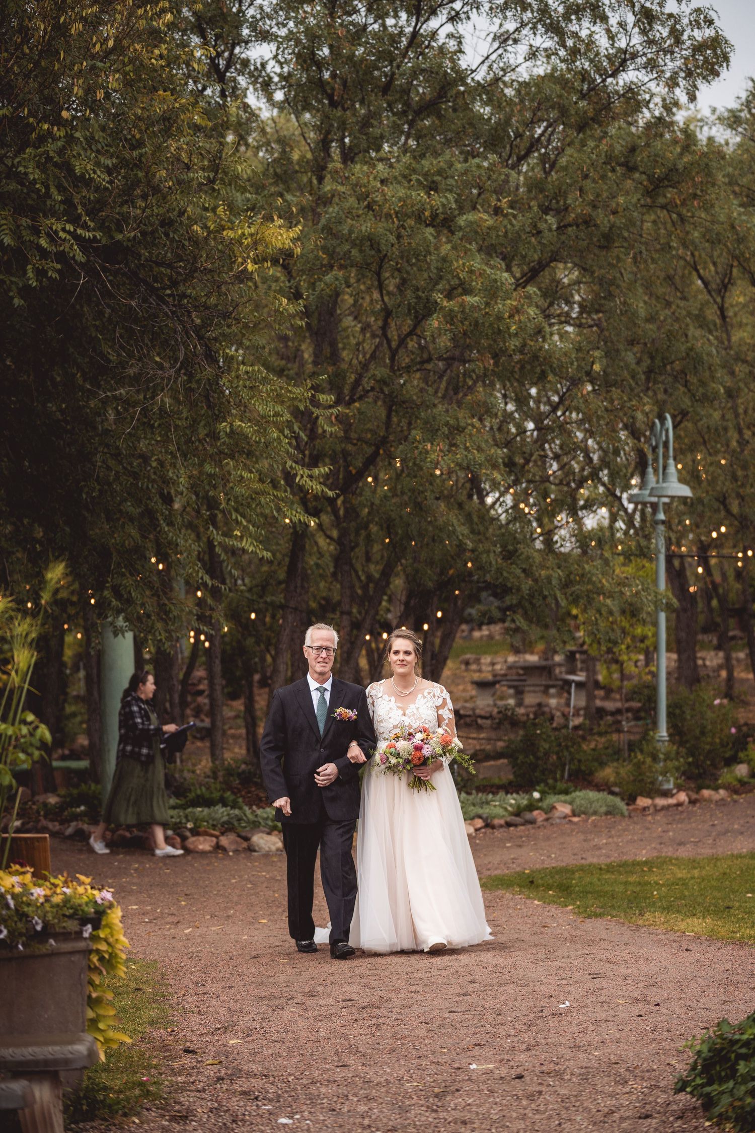 Bridal party making their way down tree-lined garden path during outdoor ceremony.