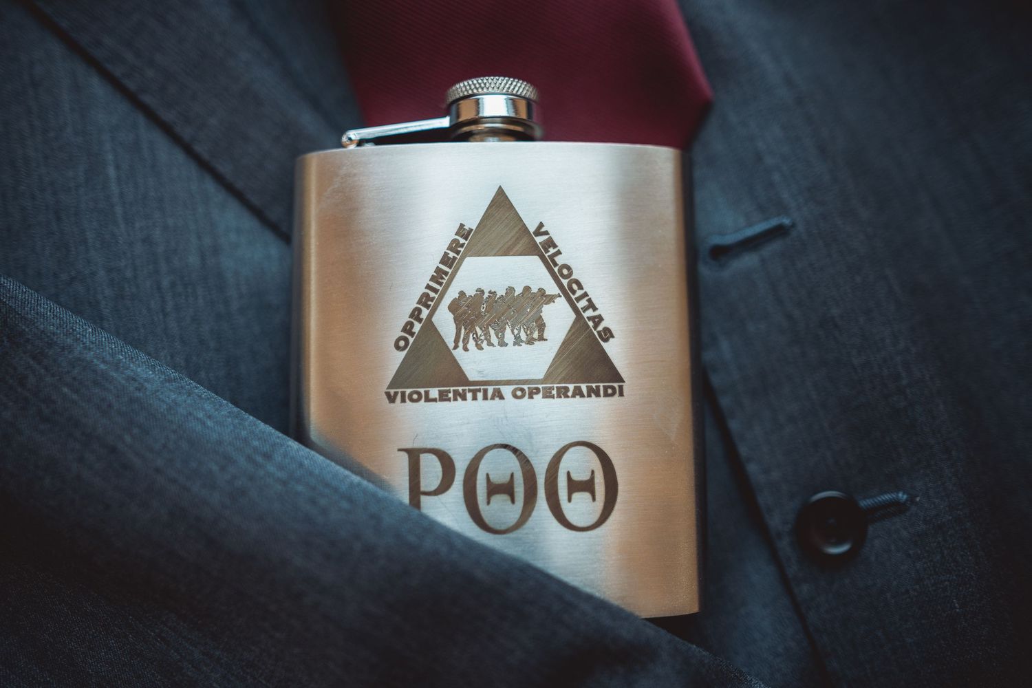 Silver flask with triangular logo design displayed against dark fabric.