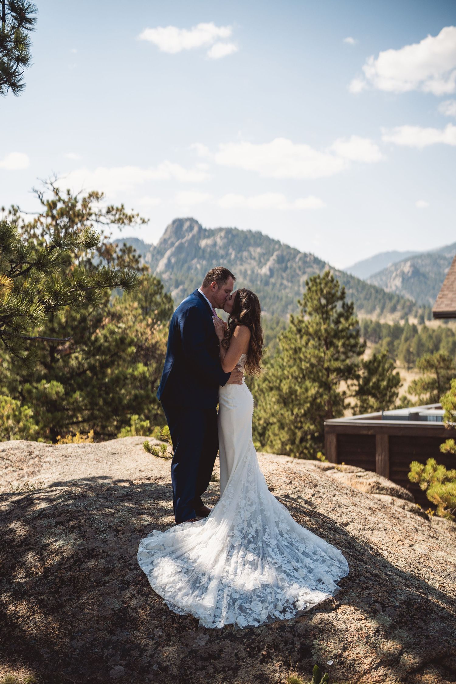 Wedding couple posing on rocky outcrop with mountain vistas and blue skies in background.