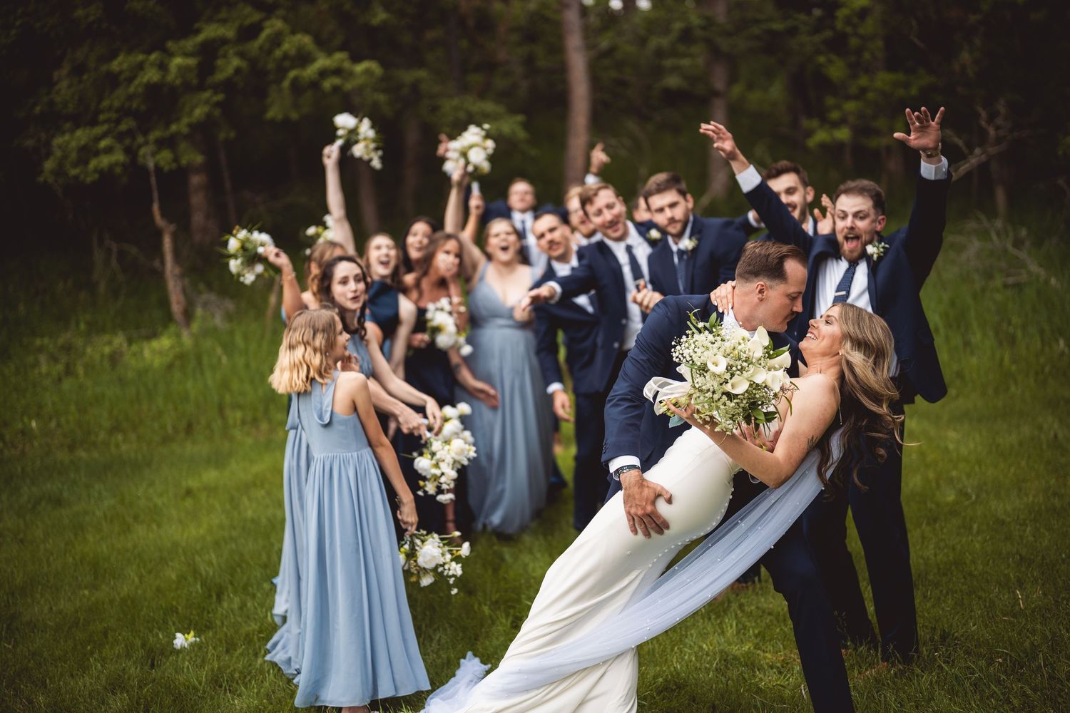 Wedding party celebrating with joy outdoors, bridesmaids wearing light blue dresses.