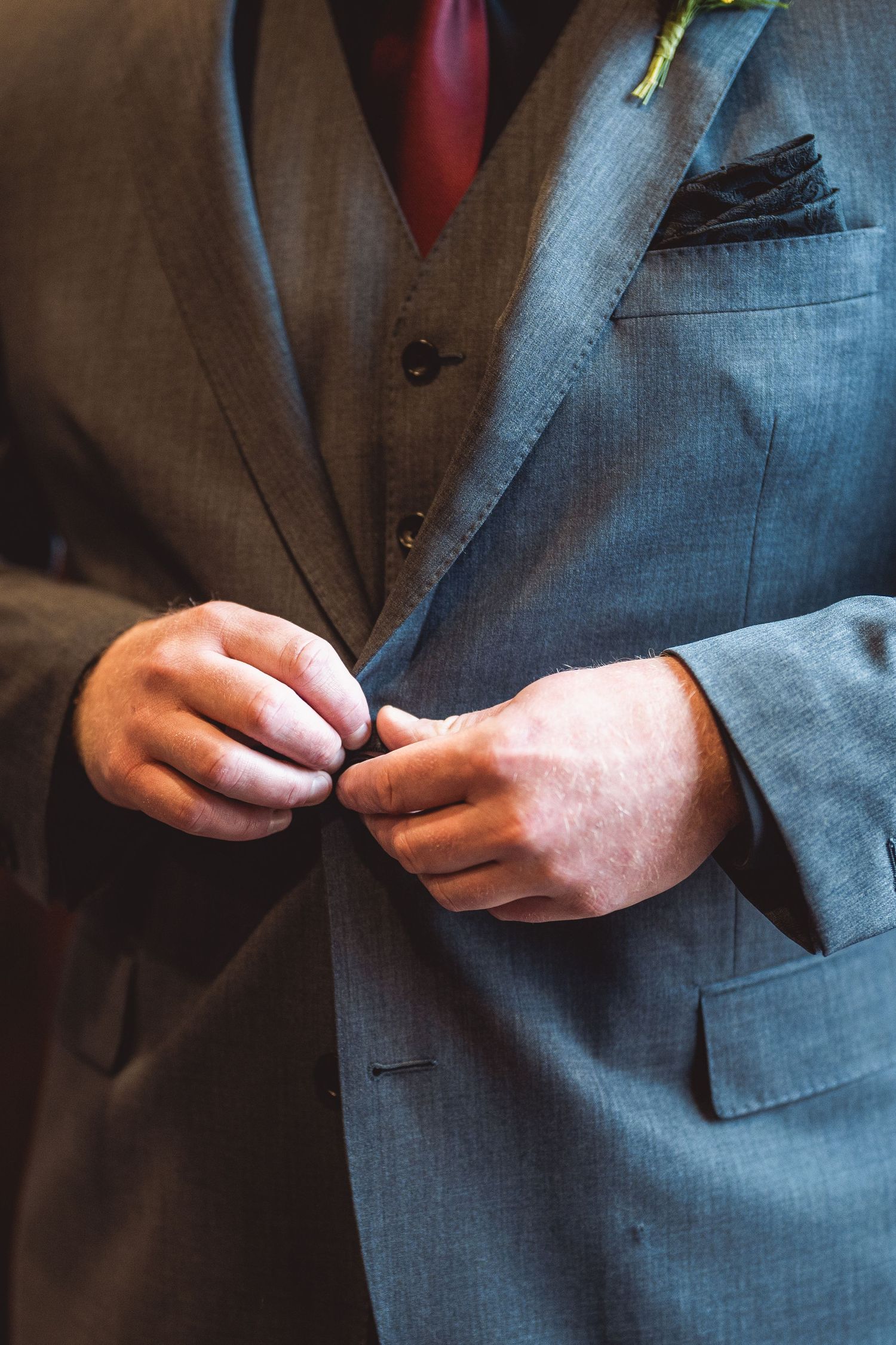Close-up sequence showing hands buttoning a grey suit jacket.