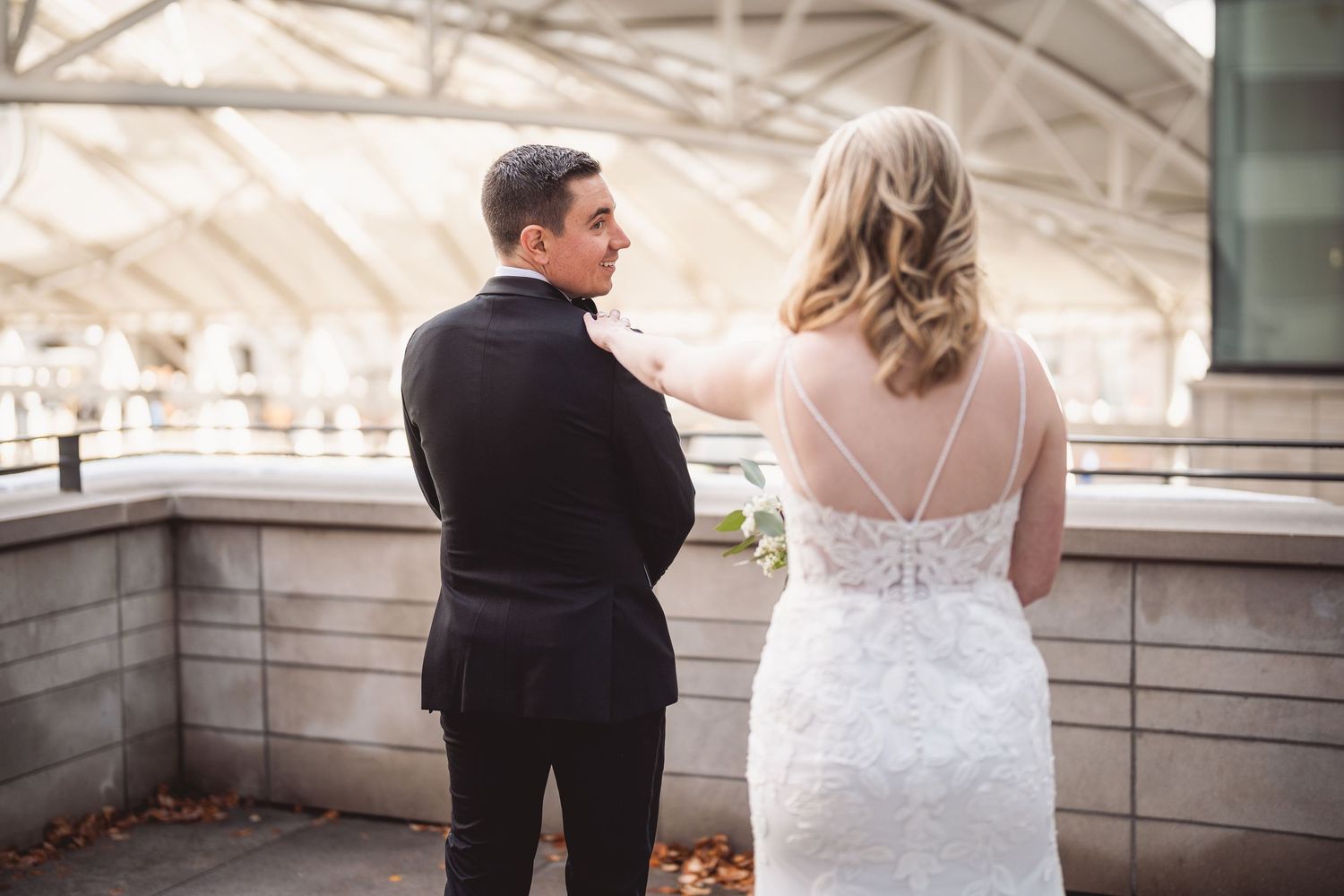 Couple in wedding attire photographed from behind on stone terrace.
