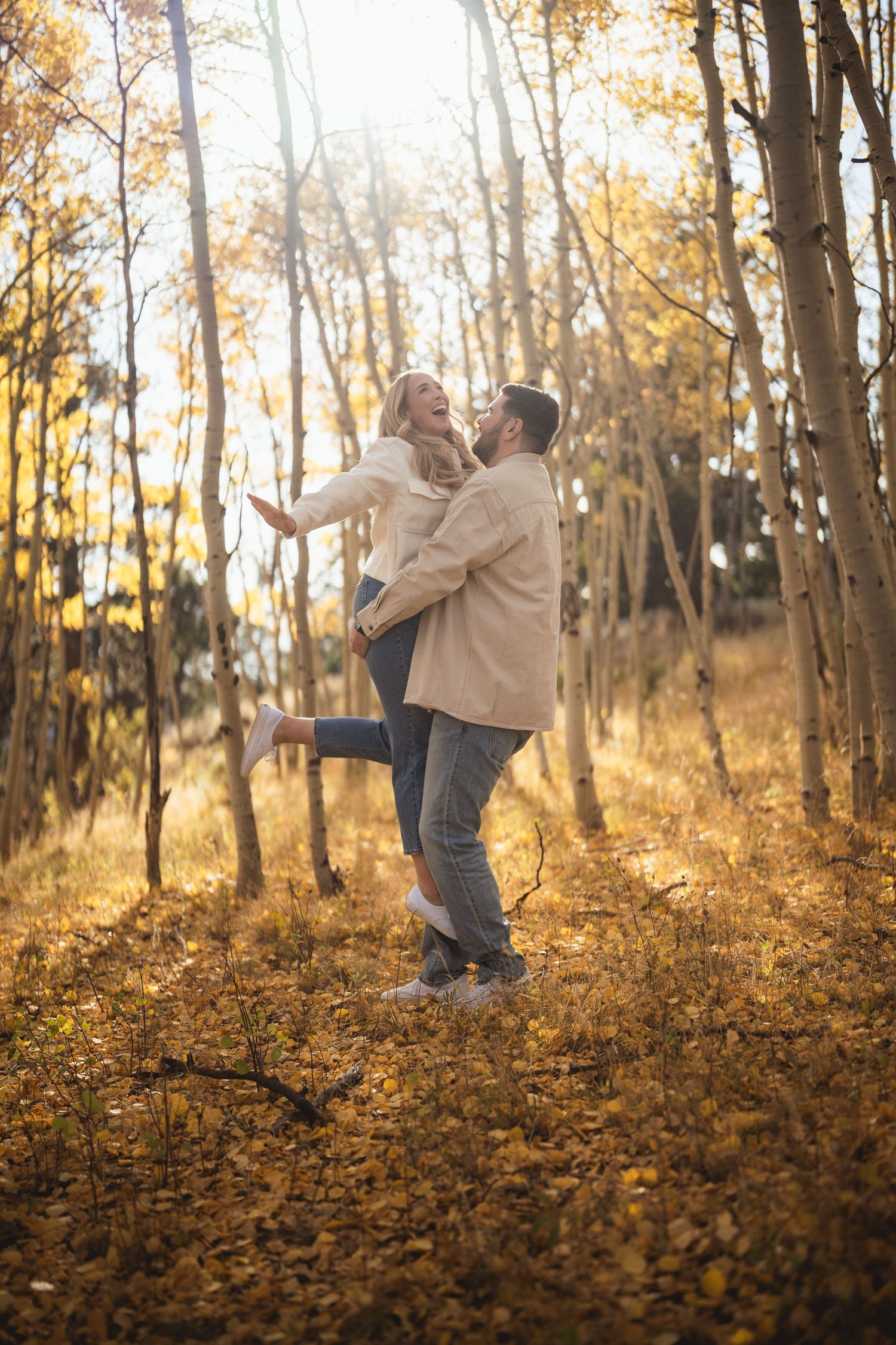 Couple in matching outfits dancing playfully among fall trees.