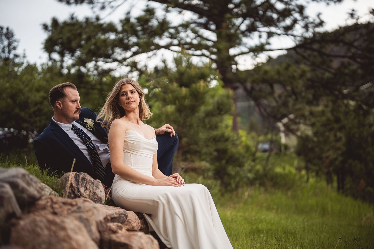 A wedding couple sits together on natural rock formations surrounded by mountain scenery.