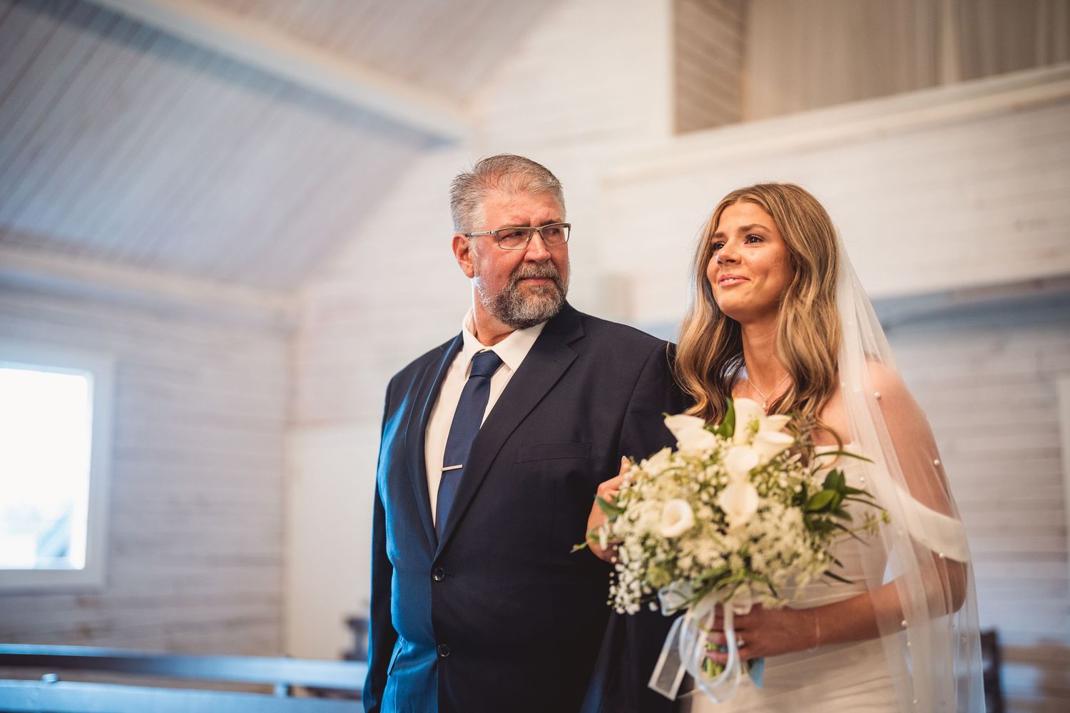 Wedding ceremony inside traditional white chapel with elegant lighting and vaulted ceilings.