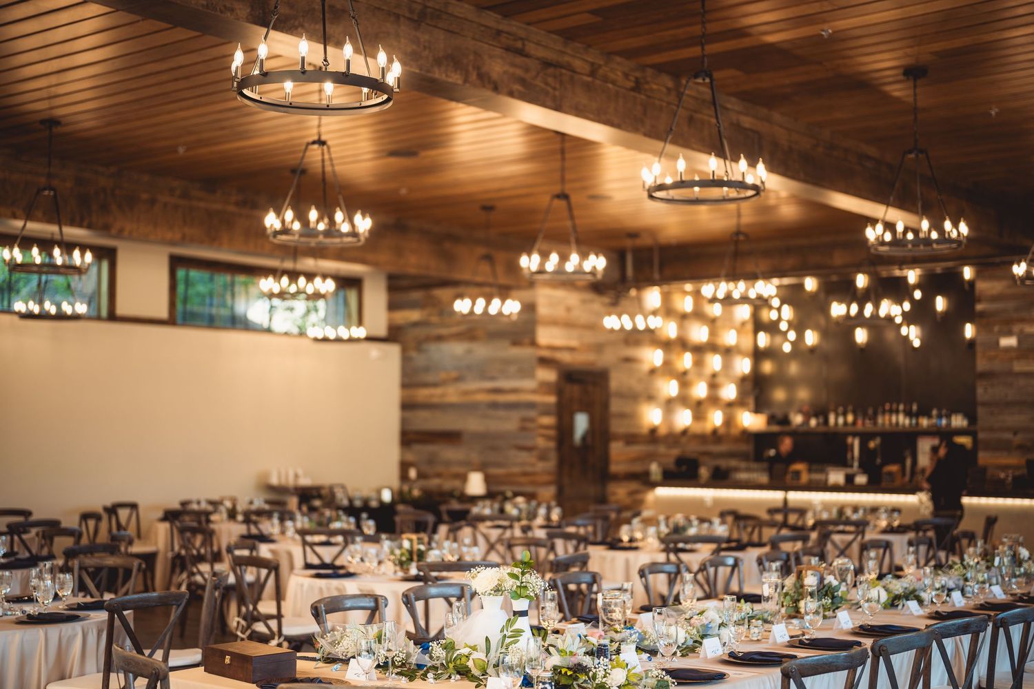 A rustic wedding reception venue with string lights and wooden ceiling beams.