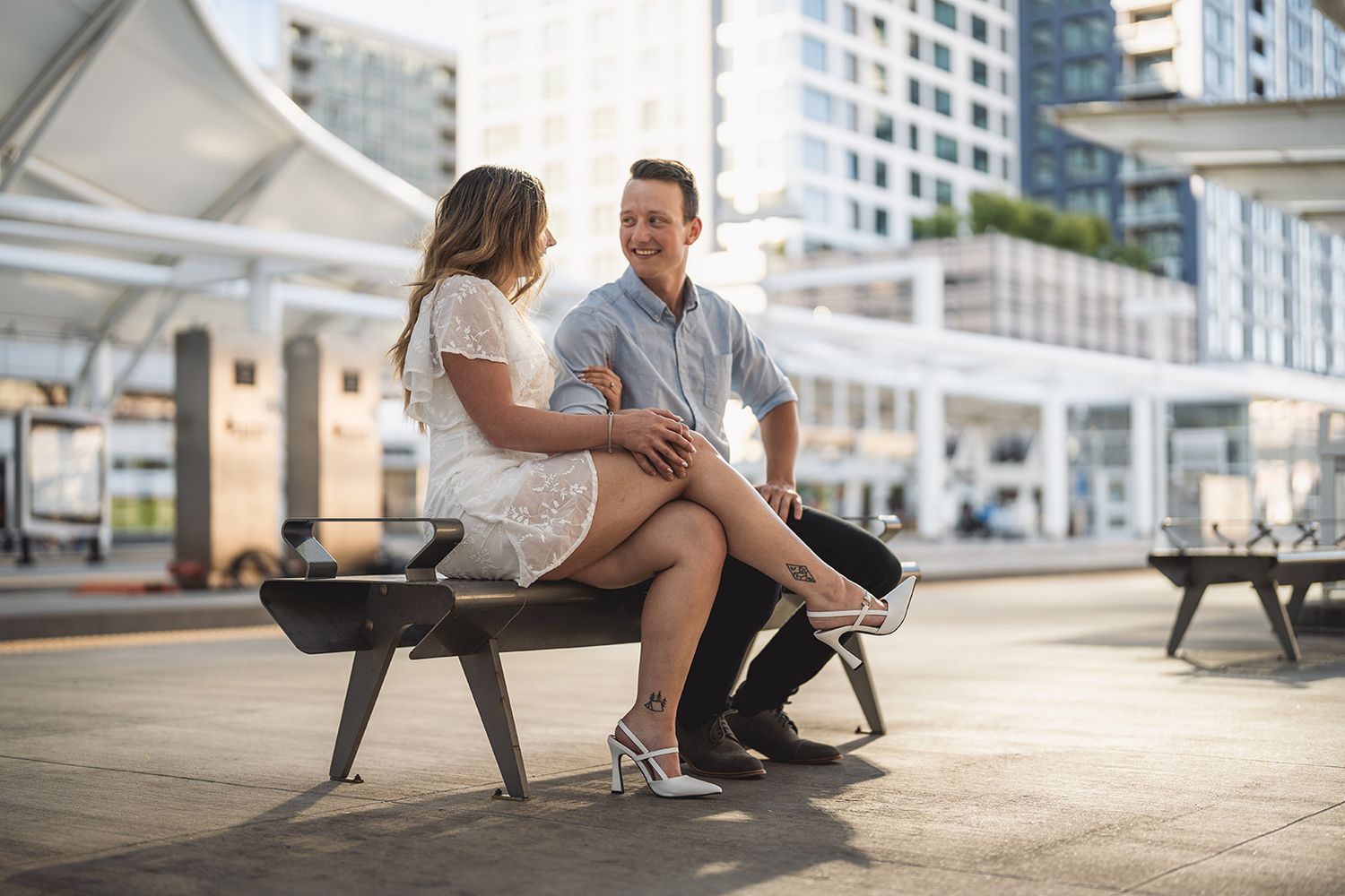 Stylish couple poses together at modern urban location with tall buildings in background.