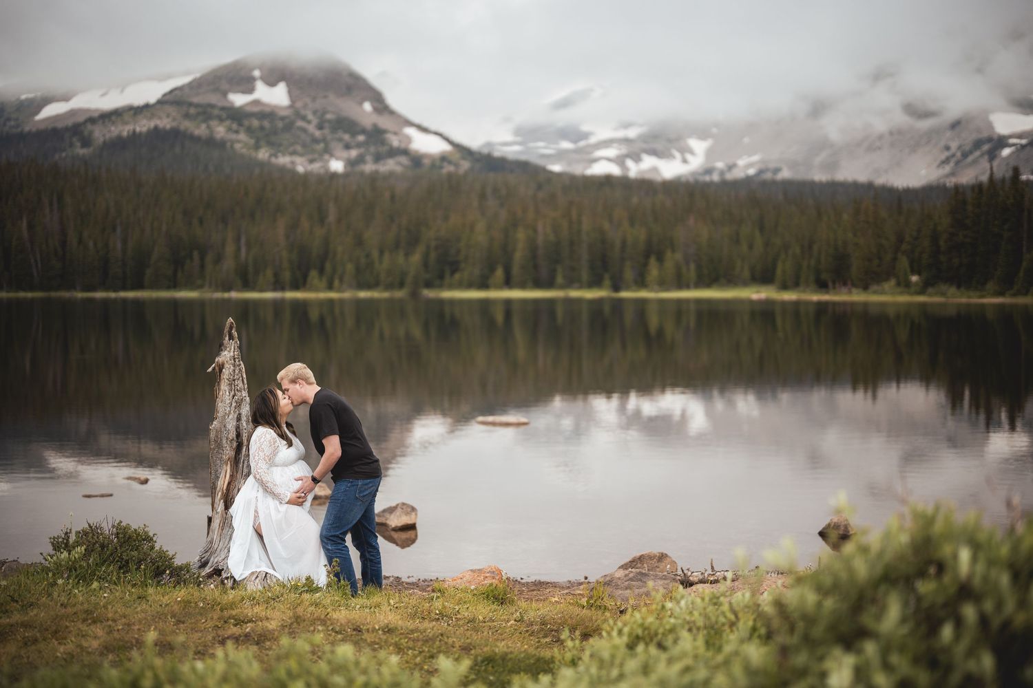 Panoramic mountain lake view with snow-capped peaks and evergreen forest.