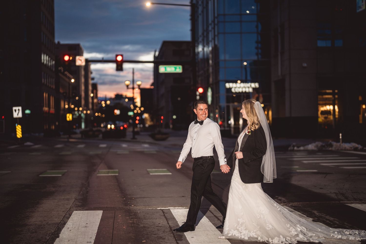Newlyweds stroll through an urban cityscape at twilight after their wedding ceremony.