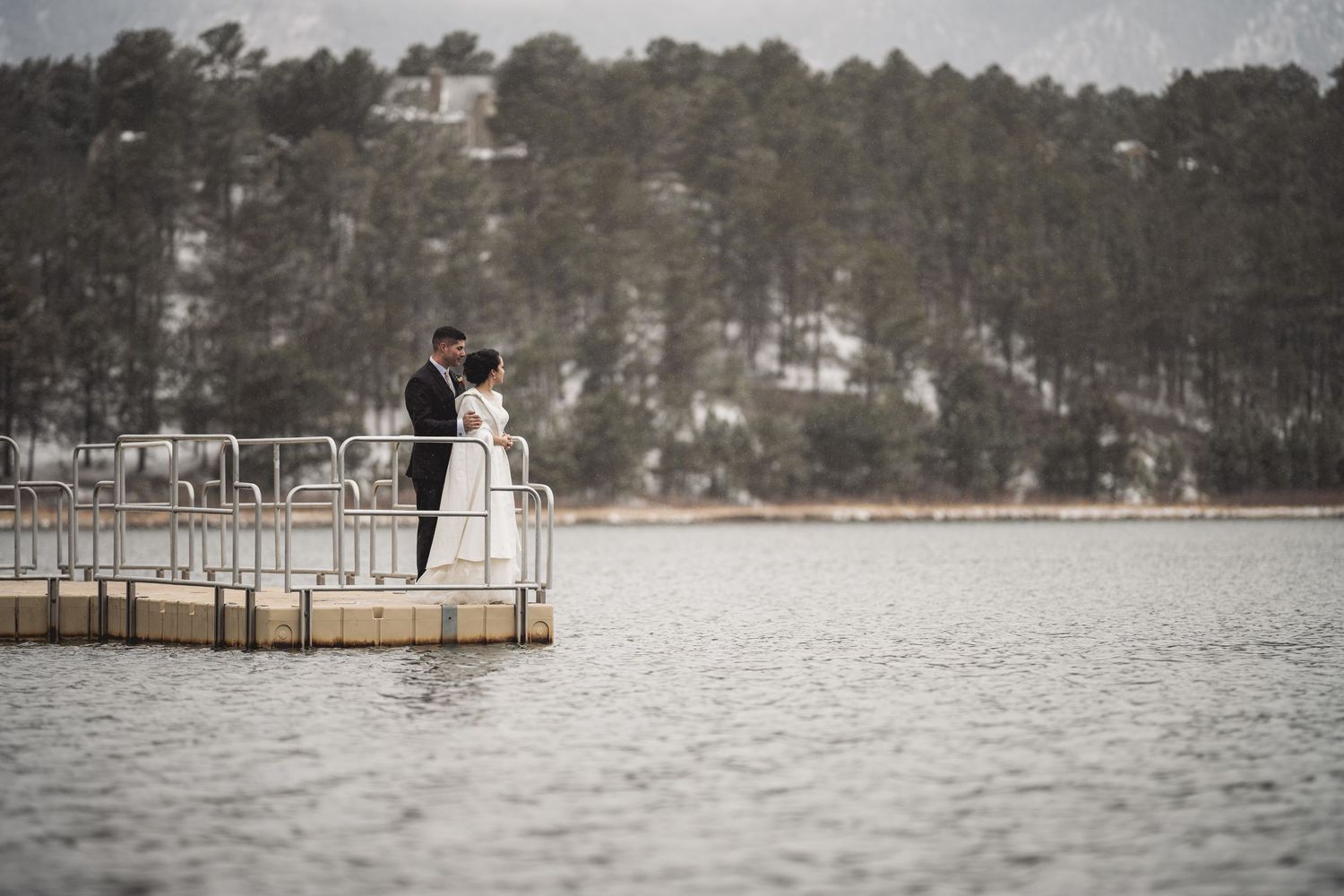 Serene lakeside dock with pine trees reflecting on calm waters.
