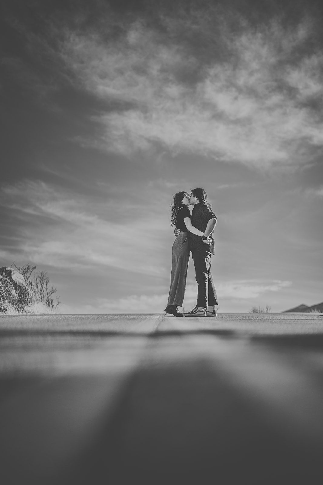 Silhouetted figures embrace against dramatic cloudy sky in black and white photography.