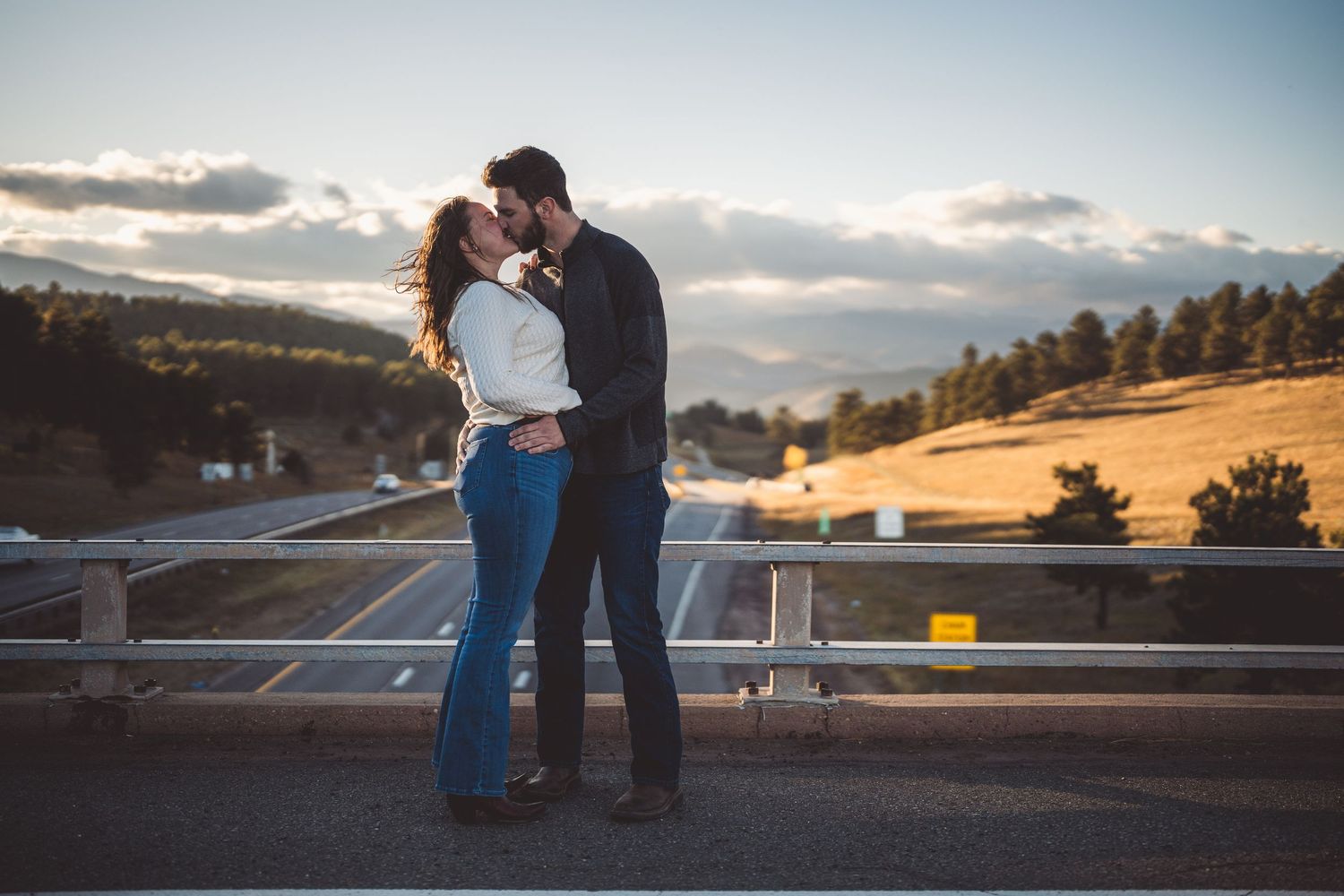 A tender moment shared on an overlook with mountain scenery and clouds at sunset.