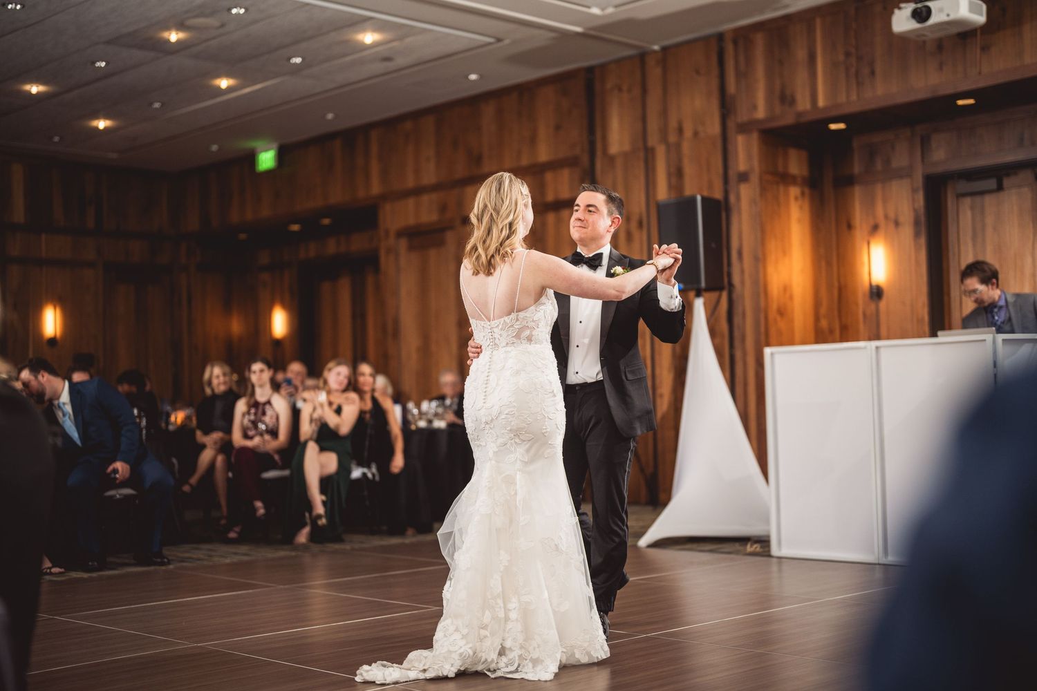 Couple dancing in a spacious wood-paneled ballroom with decorative white panels.