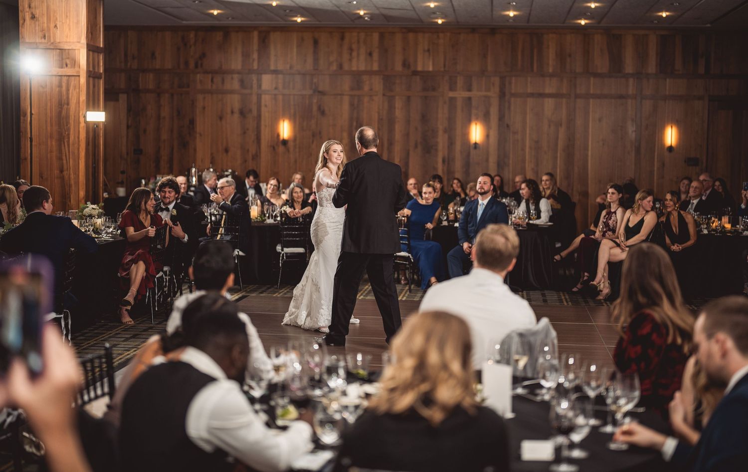 Panoramic view of wedding reception with guests seated at tables in a wood-paneled ballroom.