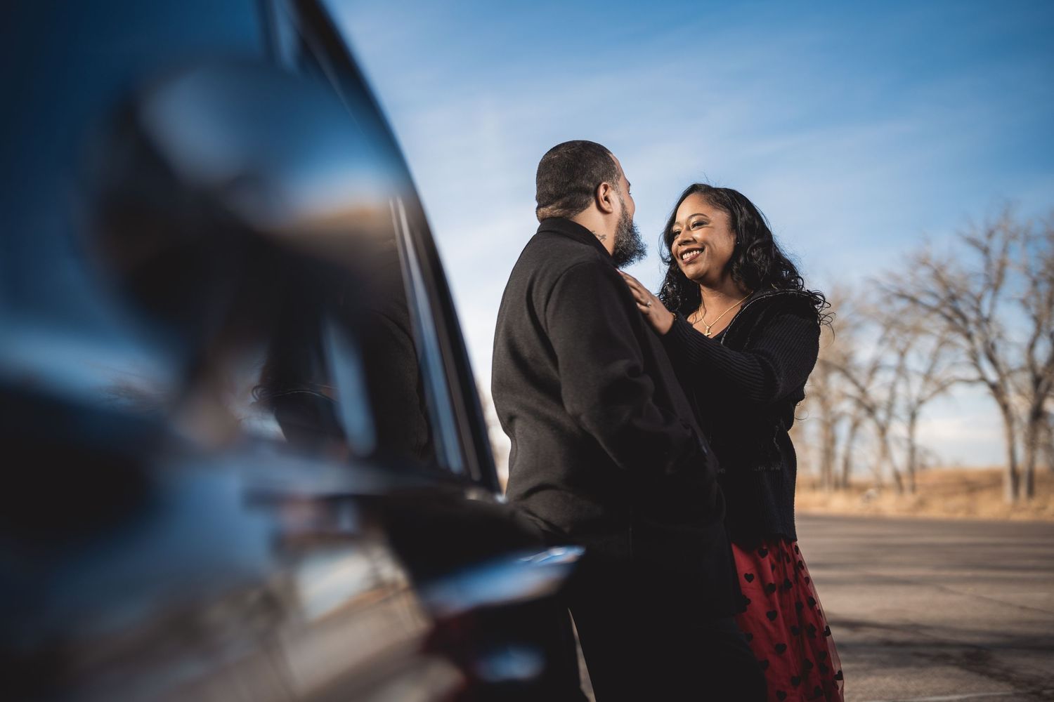 A couple shares intimate moments near a classic car during their engagement photoshoot.