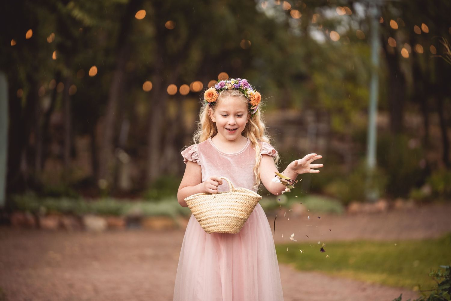 Person in pink dress scattering flower petals along garden path with twinkle lights.