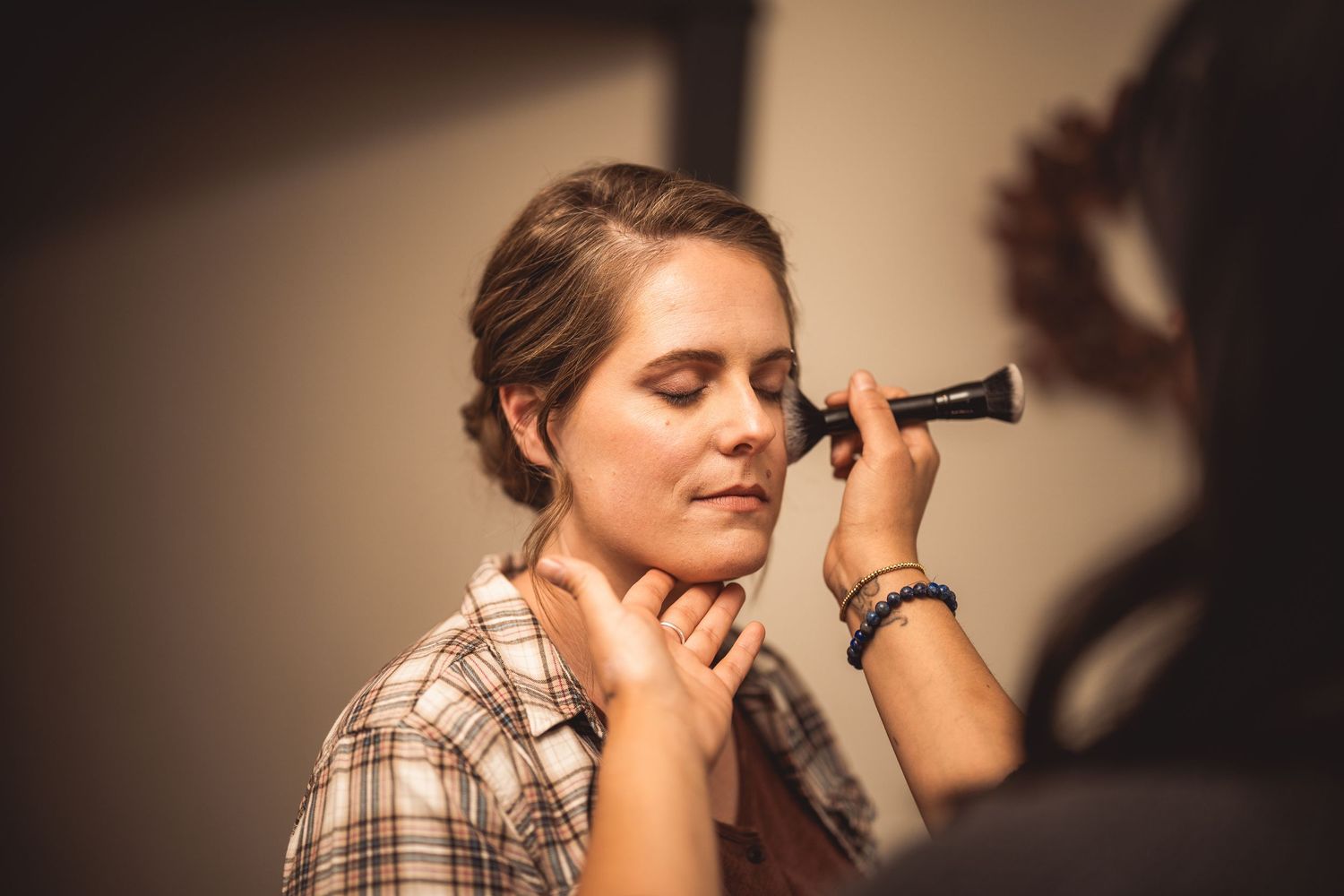 Makeup artist applies cosmetics in moody lighting with soft focus.