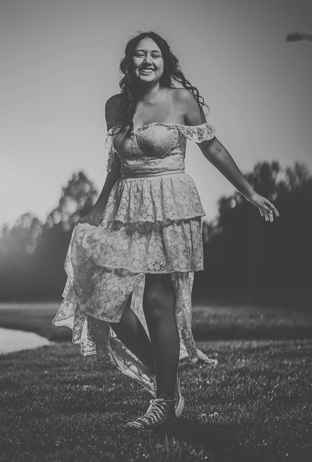 Person wearing a delicate lace dress dancing playfully in a field in black and white.