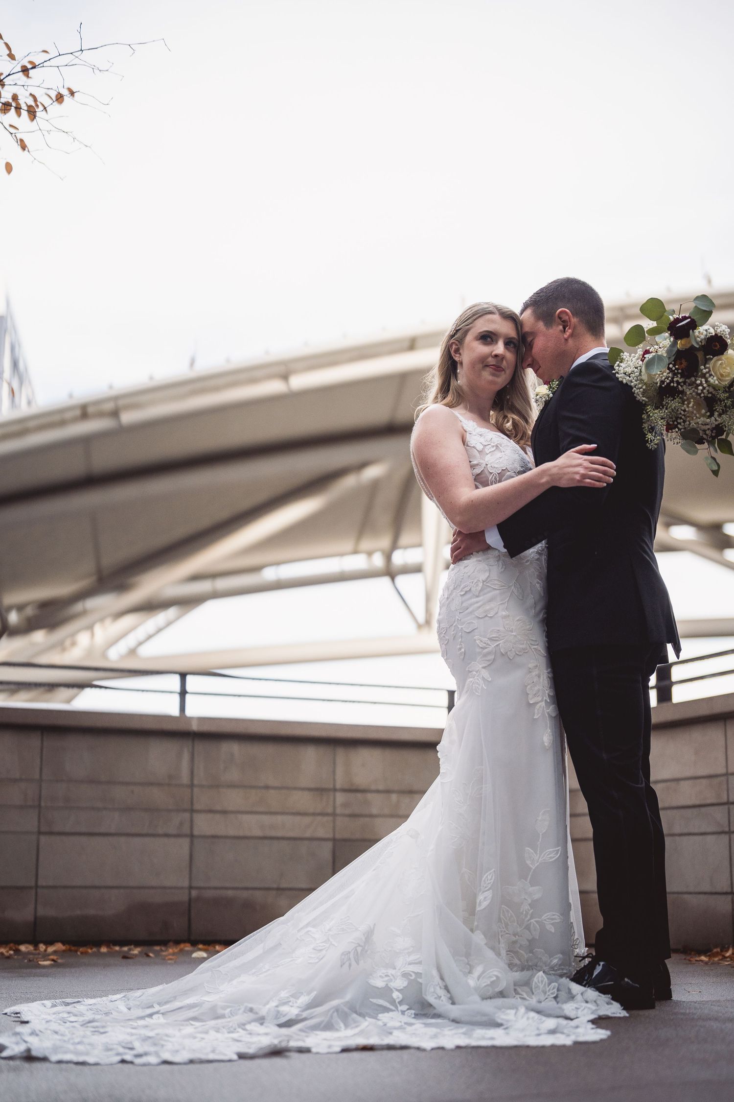Wedding couple in formal attire embraces on outdoor terrace with train of dress flowing.