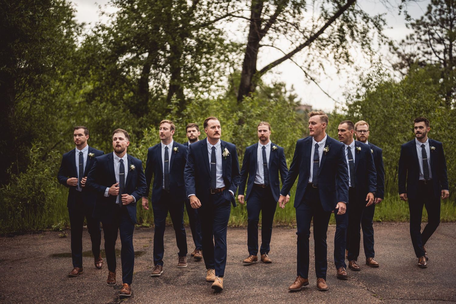 Groomsmen in matching navy suits walking in formation outdoors.