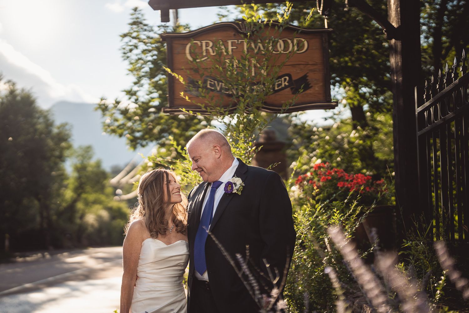 Couple shares romantic moment under Craftwood Inn sign surrounded by lush greenery and mountains on their wedding day.