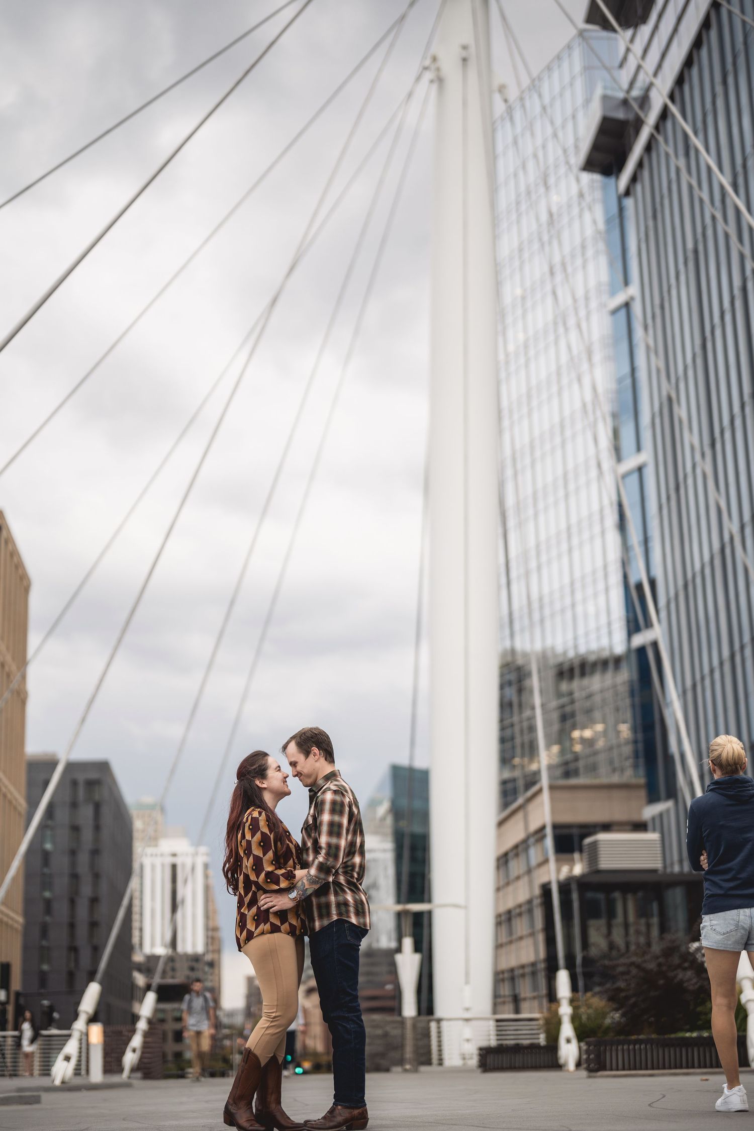 Couple sharing a romantic moment in an urban setting with a suspension bridge and modern skyscrapers in the background.