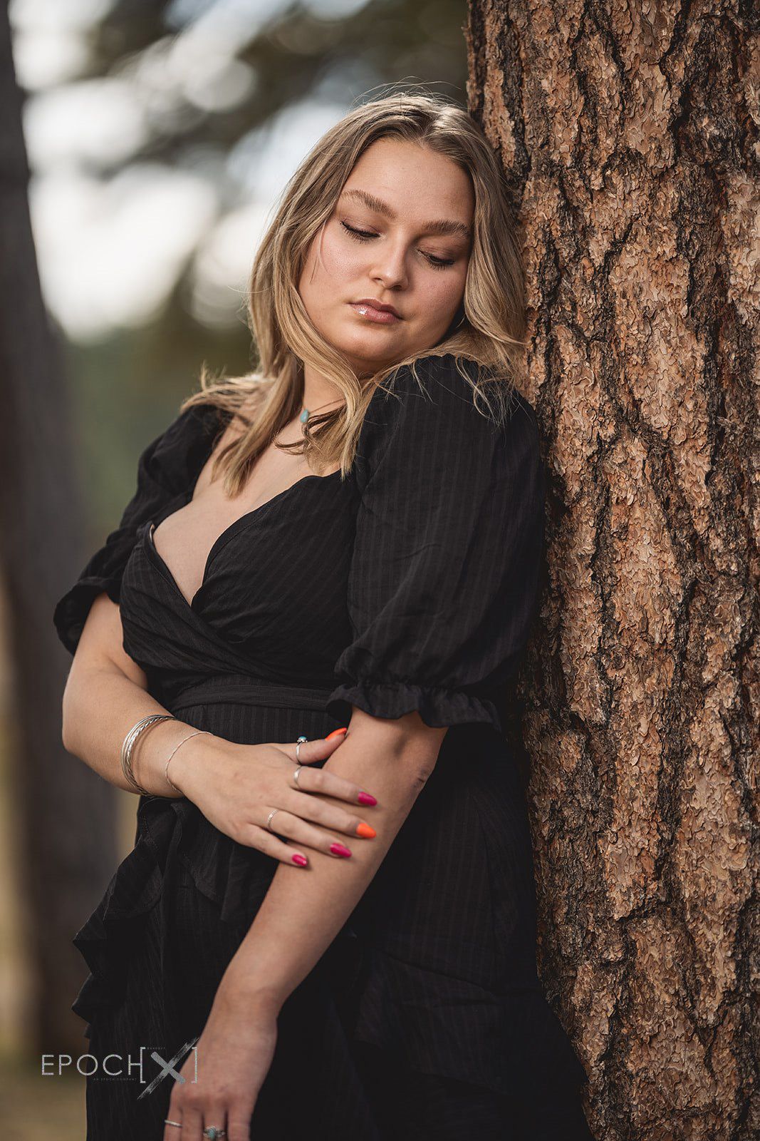 Romantic couple in black clothing embracing against a rustic tree trunk.