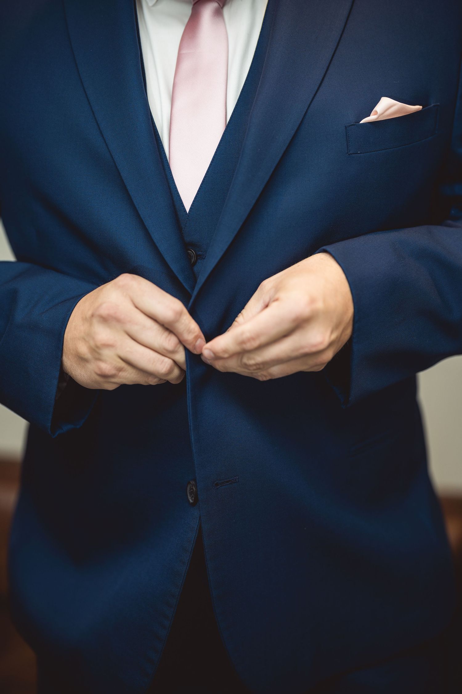 Navy blue suit jacket being buttoned with pink tie visible.