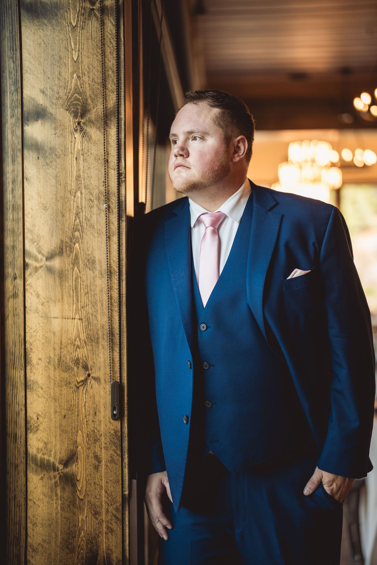 Person in blue suit leaning against rustic wooden post with warm lighting.