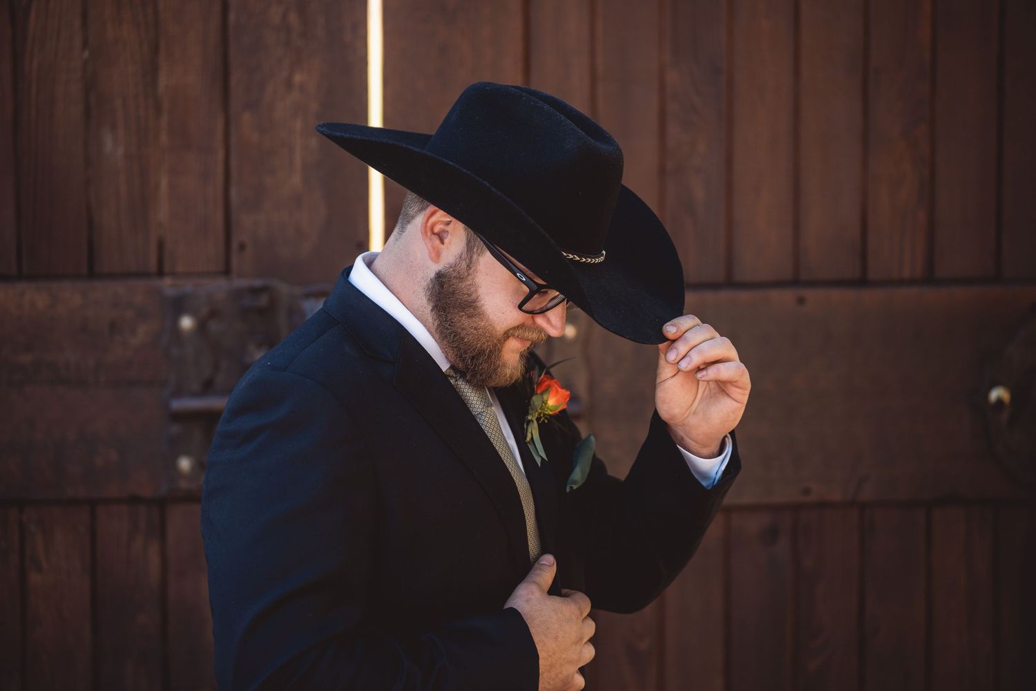 Row of groomsmen in black suits and cowboy hats against wooden backdrop.