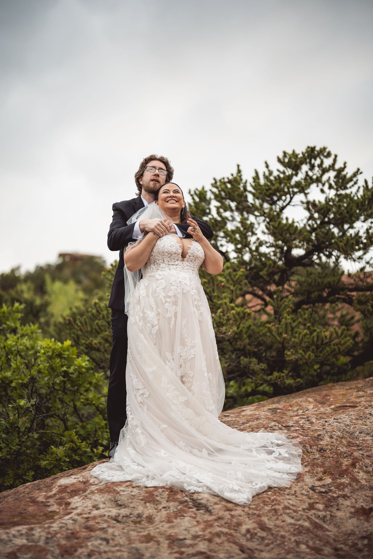Newlyweds share an intimate moment on a mountain overlook with a dramatic lace wedding dress train.
