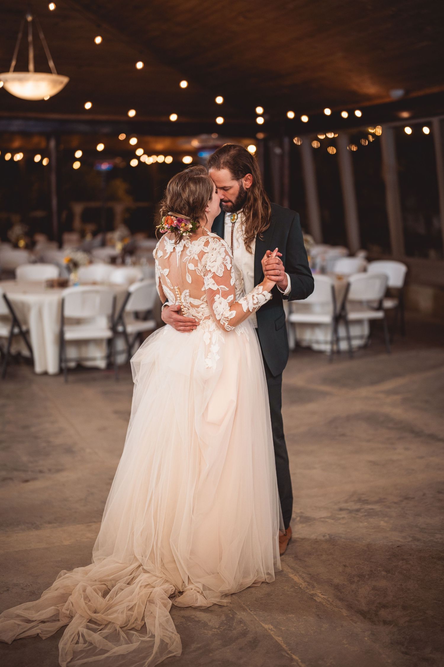 Intimate wedding dance in a rustic venue with ambient lighting and white table settings.