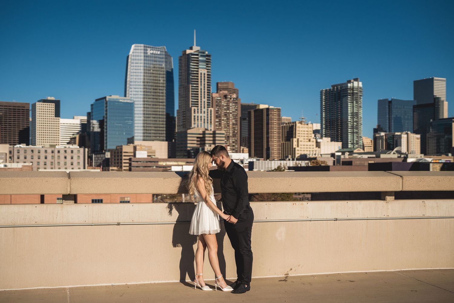 Couple sharing a romantic moment on a rooftop with the Dallas city skyline in the background on a sunny day.