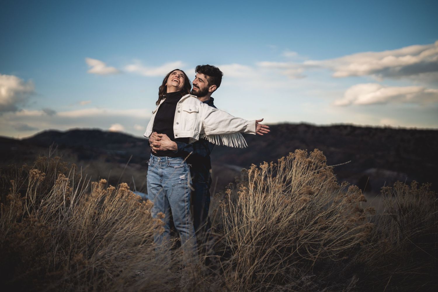 Silhouetted couple embracing against scenic mountain landscape at sunset.