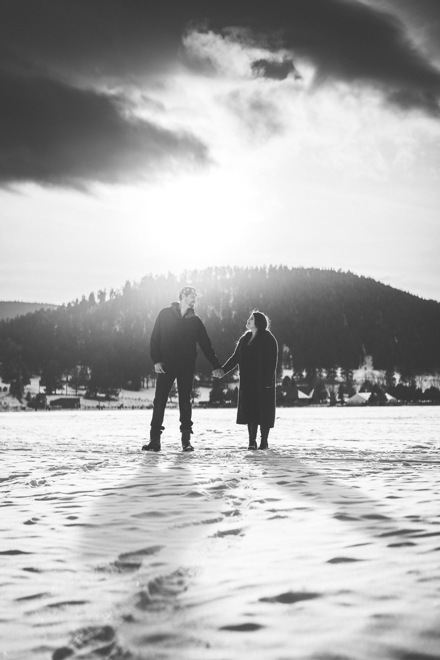 Silhouettes of people standing in snowy landscape with dramatic cloudy sky and mountains.