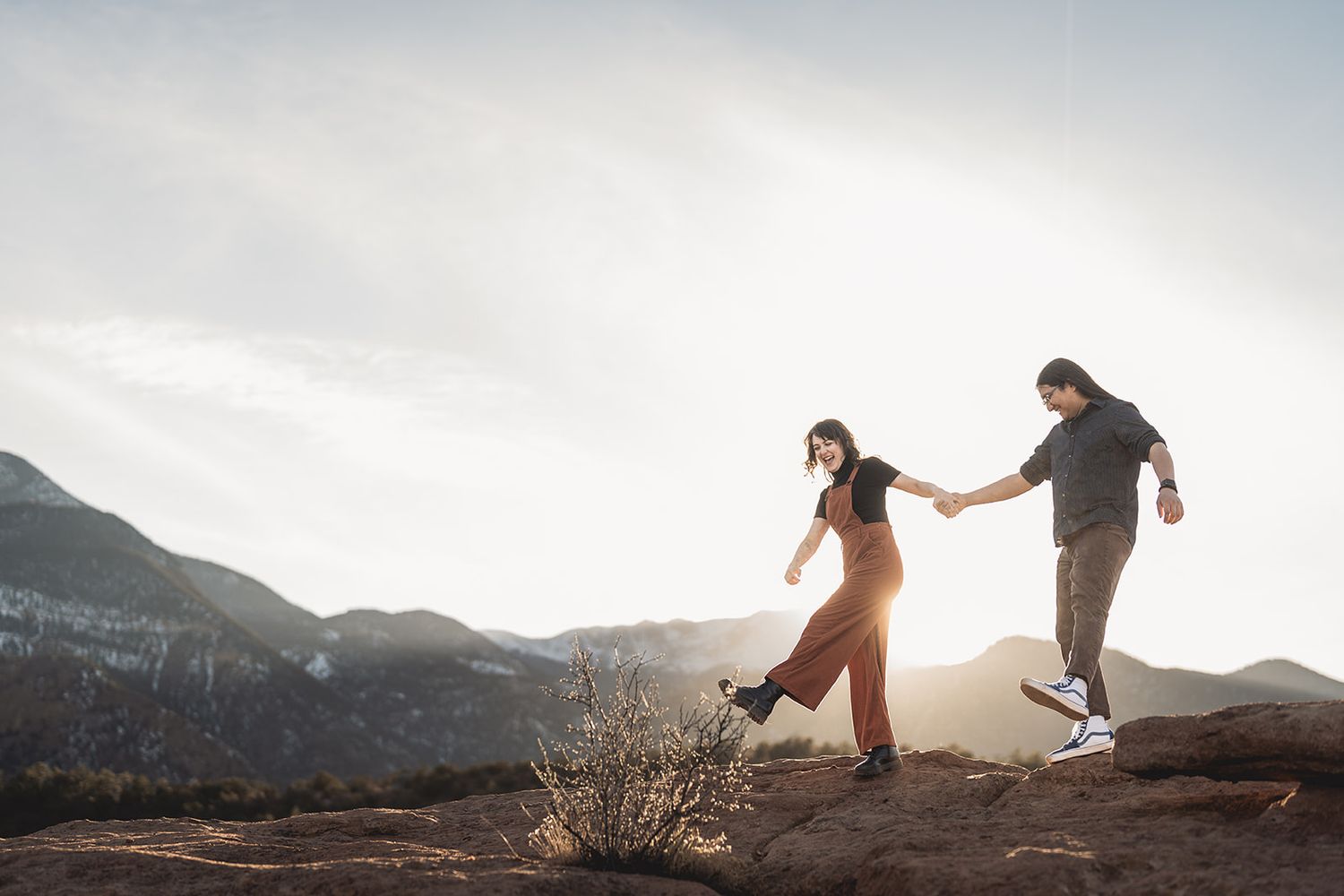 Two people playfully run and dance together on mountaintop during golden hour.