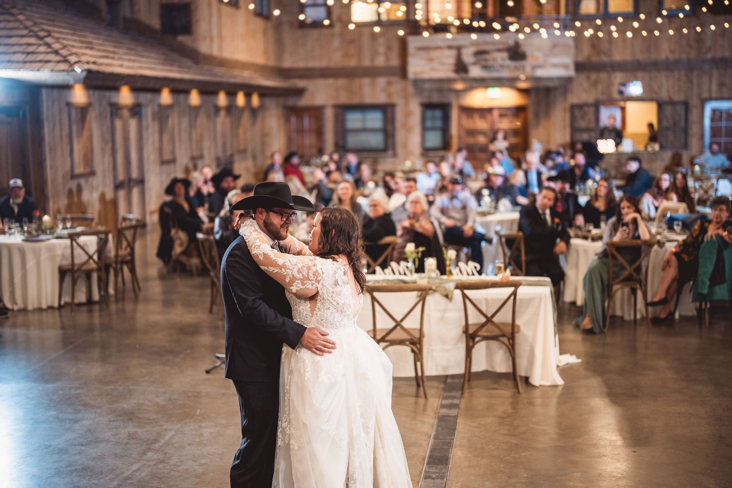Wedding reception first dance in spacious rustic venue with string lights and wooden details.