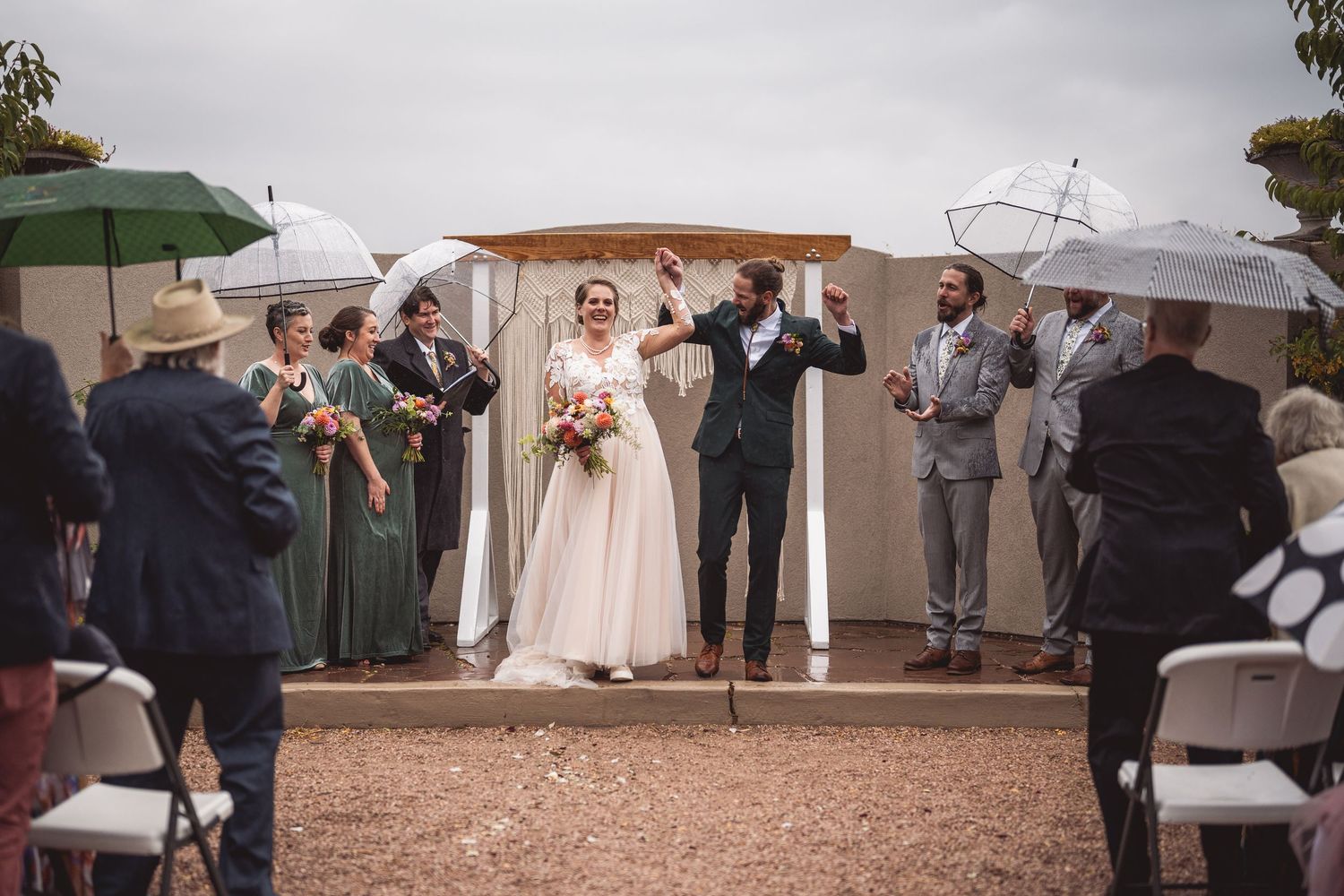 Panoramic view of rainy wedding ceremony with white umbrellas and stucco walls.