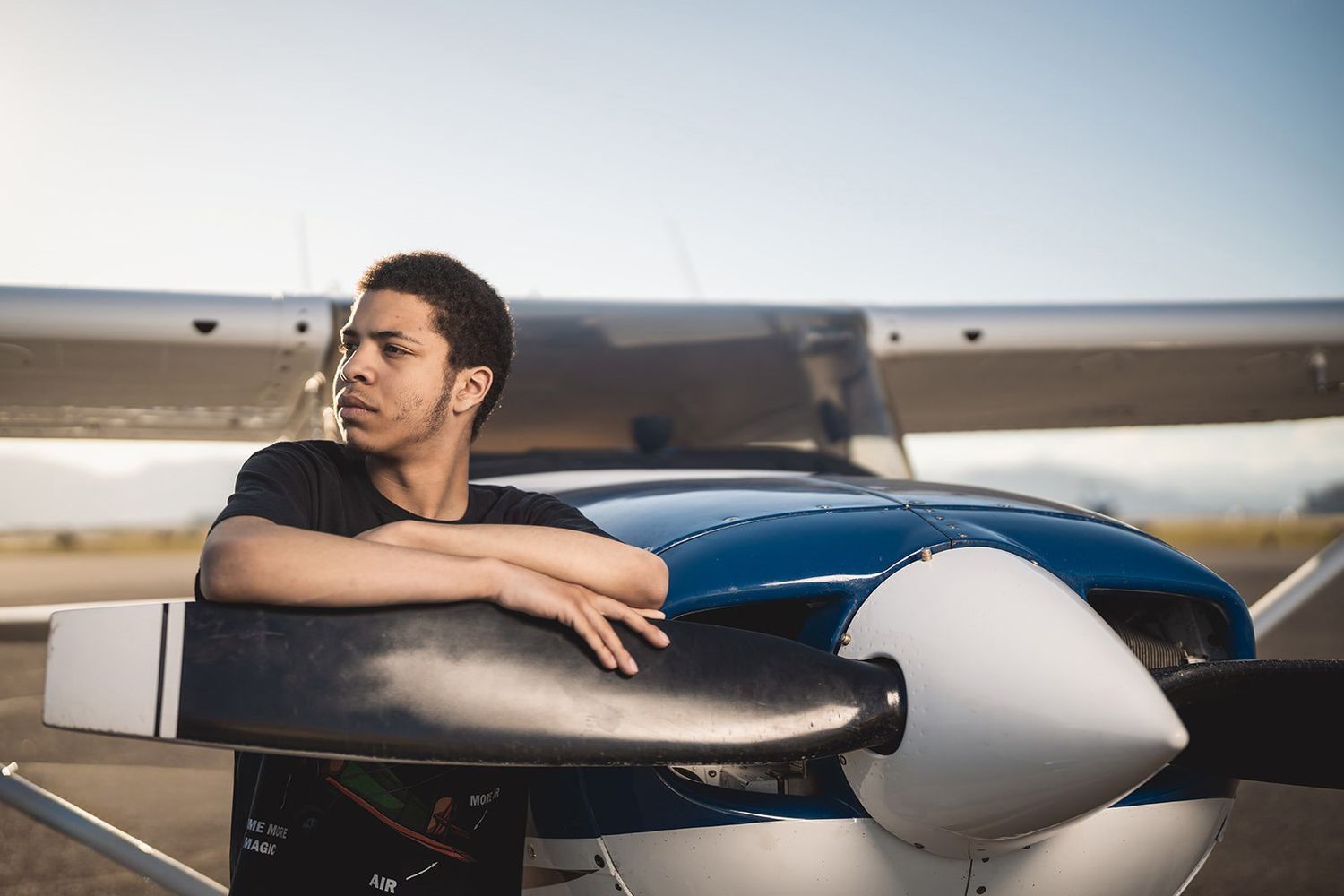 Person leaning on wing of small private aircraft on airport runway.