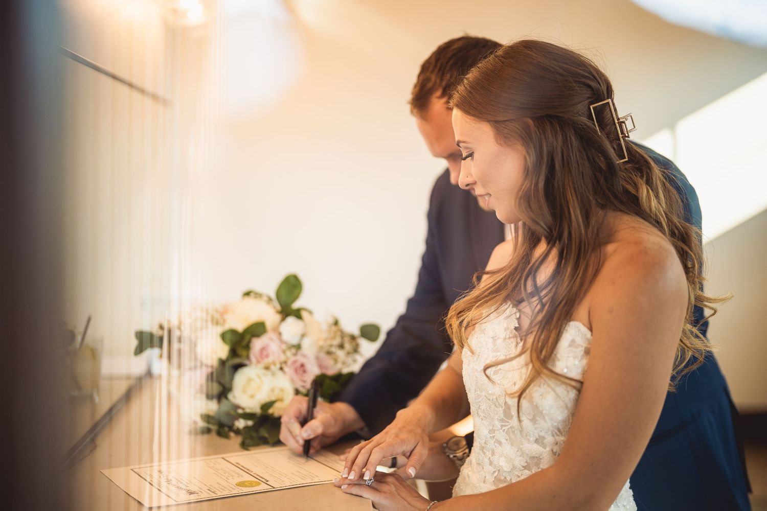 Couple signing marriage documents at elegant indoor wedding ceremony.